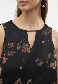 Černý bezrukávový top s výstřihem do V, zdobený květinovým vzorem v tlumených růžových a zelených tónech a úzkým klíčová otvorem.