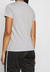 Grå bomullströja med rund halsringning och korta ärmar, med en figursydd design och mjuk textur. Bärs tillsammans med svarta byxor.