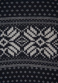 Mörk stickad tyg med ett geometriskt mönster i ljusgrått, med växlande designer av diamant- och zigzagformer.