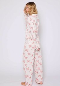 Pyjamastel met lange mouwen gemaakt van zacht stof, met een witte achtergrond en rode strikpatronen, losse broek en knoopsluiting.