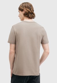T-shirt corta beige in cotone, con colletto rotondo, design semplice, e vista posteriore che evidenzia la cucitura della spalla e la trama morbida.