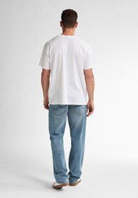 Tricou alb din bumbac, cu mâneci scurte, asortat cu blugi din denim bleu deschis. Blugii au buzunare standard și o croială lejeră.