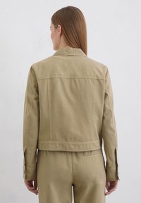 Khaki jeans jakna s strukturiranim ovratnikom, dugim rukavima i dugmadima na manžetama. Ima šav na leđima i skraćeni siluetu.
