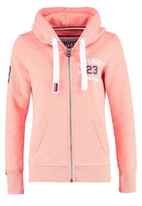 Felpa con zip color corallo e rosa con cordini bianchi, tasche frontali, polsini e bordi a costine, e testo "Superdry 23 Athletic" sul petto e sulla manica.