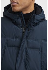 Navy lightweight puffer jacket with a hood, zip closure, and snap details; features quilted texture and two front pockets.