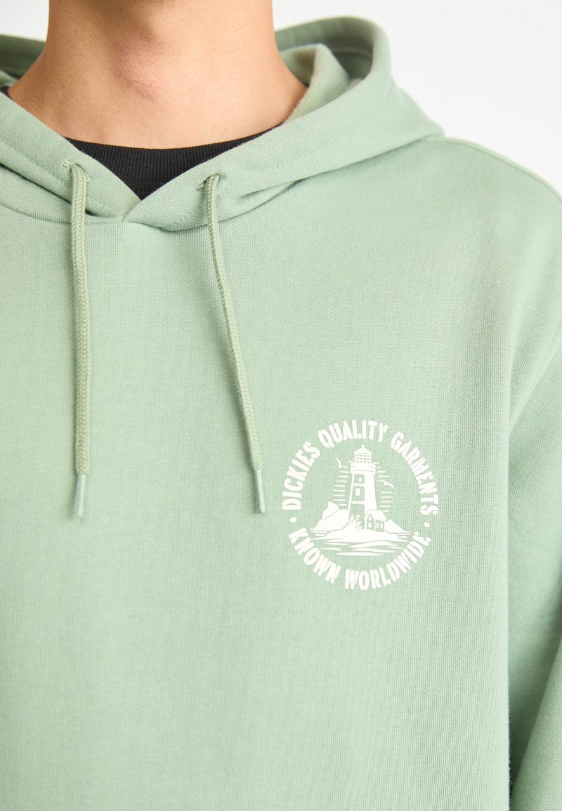 Light green hoodie made of soft fabric with a kangaroo pocket, featuring a white circular logo with a lighthouse design on the front.