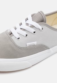 Szürke vászon sneaker fehér fűzővel, gumitalppal és varrott díszítéssel. Az oldalán logófolt, valamint lekerekített orrdesign jellemzi.