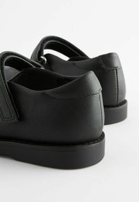 Chaussures en cuir noir avec une texture lisse, une forme arrondie et une semelle plate, dotées de panneaux élastiques sur les côtés et de détails cousus.