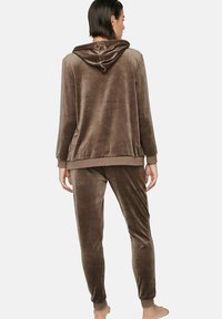 Ensemble de détente en velours marron comprenant une veste à capuche et un pantalon fuselé. Texture douce avec poignets et taille élastiques pour un confort optimal.