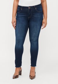Dark blue skinny jeans with a five-pocket design, frayed hem, and copper hardware; worn with pointed leopard print heels.
