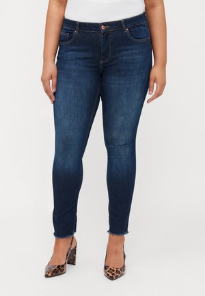 Jeans skinny blu scuro con design a cinque tasche, orlo sfilacciato e hardware in rame; indossati con tacchi a punta in stampa leopardata.
