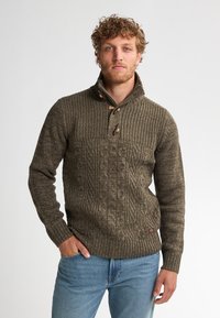 Pulover tricotat în verde măsliniu, cu un model de tricotat în cablu, guler înalt și nasturi din lemn tip toggle. Mânile și tivul cu model rib.