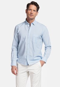 Lichtblauw overhemd met lange mouwen, borstzak en witte knopen. Gekleed met witte broek, met een casual pasvorm.