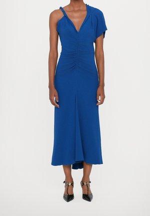 Niebieska sukienka bez rękawów z dekoltem w serek, marszczonym przodem i asymetrycznym wzorem na ramionach. Sięga poniżej kolan. Połączona z czarnymi szpilkami.