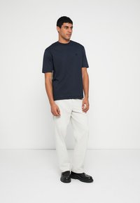 Navy short-sleeve t-shirt in cotton blend, featuring a crew neckline and a small logo detail on the chest, paired with light-colored pants.