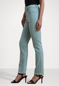 Jeans skinny de color azul claro con cintura alta, que cuentan con cinco bolsillos y una cremallera en la bragueta. Combinados con sandalias negras de tacón.