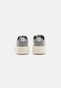 Ein Paar graue niedrige Converse All Star Turnschuhe, von hinten auf einem weißen Hintergrund gezeigt.