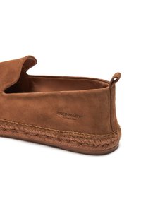 Chaussure slip-on en suede marron avec une semelle en jute tressé, présentant un design doux et arrondi, ainsi qu'une étiquette embossée avec "COLLECTION FRED MARTIN."