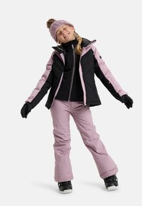 Winter ski-outfit met een zwart en lichtroze geïsoleerde jas, zwart topje, lichtroze broek, zwarte handschoenen en een gebreide roze muts.