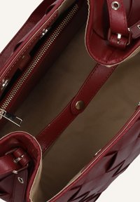 Rode synthetische leren tote bag met een binnenzak met rits, een gladde textuur en een decoratieve, gemusterde buitenkant. Een beige voering is zichtbaar.