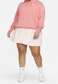 Rosa huvtröja med ficka framtill, matchat med en ljusrosa skorts. Har Nike-loggor på båda kläderna. Slät textur, avslappnad passform.