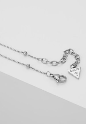 Collier chaîne en argent avec de petites perles, un fermoir mousqueton et un pendentif triangulaire gravé de "GUESS" et d'un point d'interrogation.