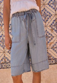 Shorts in denim azzurro chiaro con vita elasticizzata e coulisse. Presentano due tasche frontali e cuciture visibili lungo gli orli.