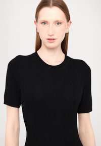 Black short-sleeve sweater with a textured pattern, featuring a round neckline and a fitted silhouette. Fabric appears soft and lightweight.
