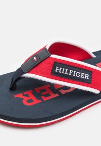 Røde og marineblå flip-flop sandaler med stofremme, gummisål og hvide detaljer. Har "HILFIGER" mærket og fed hvid skrift.