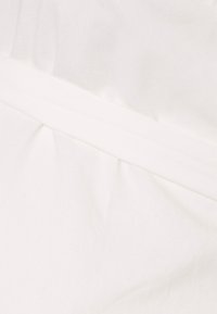 Tecido branco com uma textura suave, apresentando uma costura horizontal e um leve franzido. Design simples e minimalista.