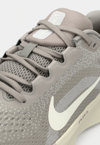 Svetlo sivi teniski zračni mrežasti gornji dio, teksturirani detalji, bež akcenti, ravne vezice i bijeli swoosh logotip sa strane.