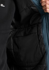 Interno di un giubbotto in pile nero, con una fodera nera uniforme e un'esterno blu in contrasto. Tasca interna visibile, con texture trapuntata.