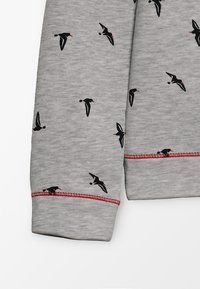 Grått tyg med svarta fågelsiluetter och röda näbbar, röd sömdetalj på ärmslut.