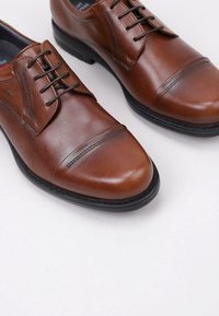 Zapatos de cuero marrón con cordones y diseño de puntera, que presentan un acabado suave, detalles cosidos y suelas de goma negras.