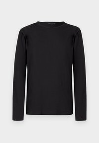 Maglietta nera a maniche lunghe con scollo rotondo e piccolo logo Tommy Hilfiger vicino al polso sinistro su sfondo uniforme.