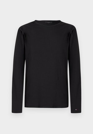 Tricou negru cu mâneci lungi și guler rotund, cu un mic logo Tommy Hilfiger lângă încheietura mâinii stângi pe fundal simplu.