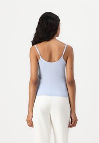 Light blue ribbed tank top with thin straps, featuring a round neckline and a fitted silhouette, paired with white wide-leg pants.