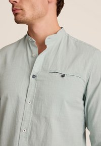 Lichtgroene, langsl sleeve shirt met een mandarin kraag, knopen aan de voorkant en een borstzak. Geverfd stof met subtiele patroondetails.