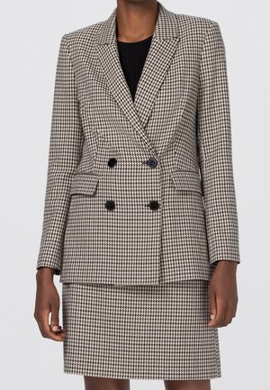 Femme portant un blazer croisé à carreaux marron et blanc avec des boutons noirs et une jupe assortie jusqu'au genou.