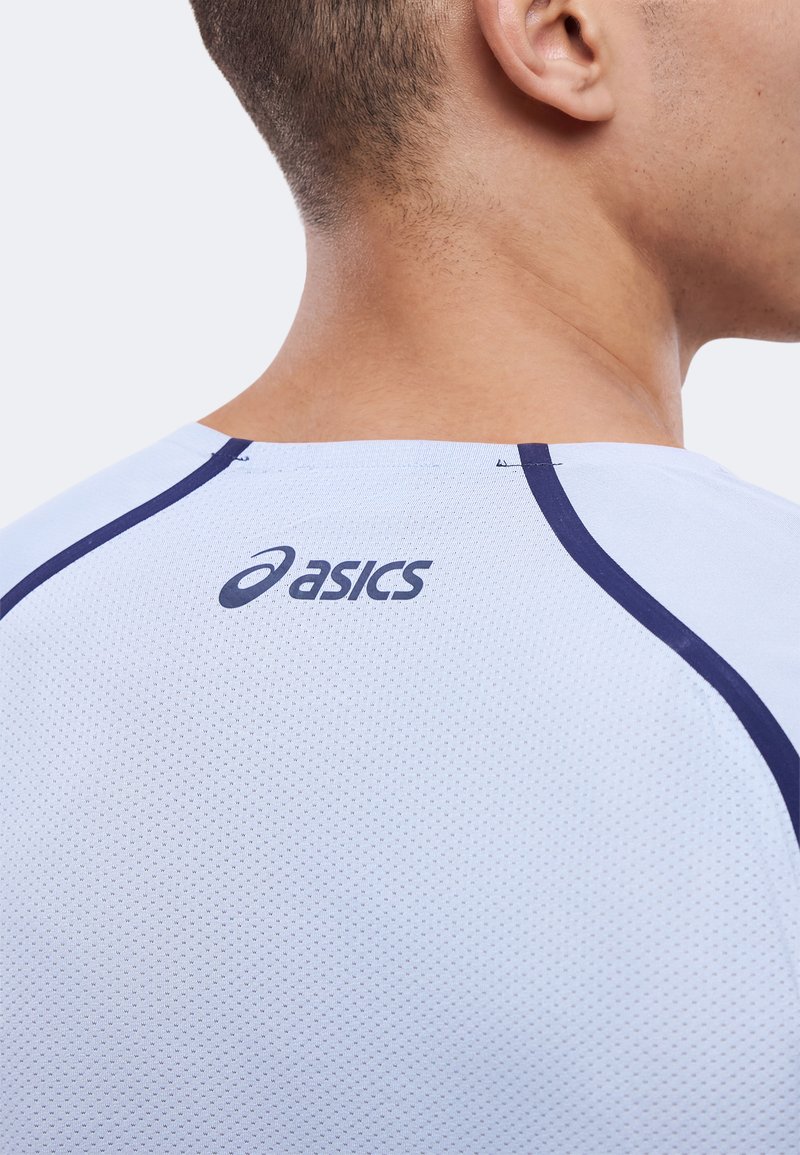 Nærbillede af bagsiden af nakken og skulderområdet på en person iført en hvid Asics sportstrøje med marineblå syninger.