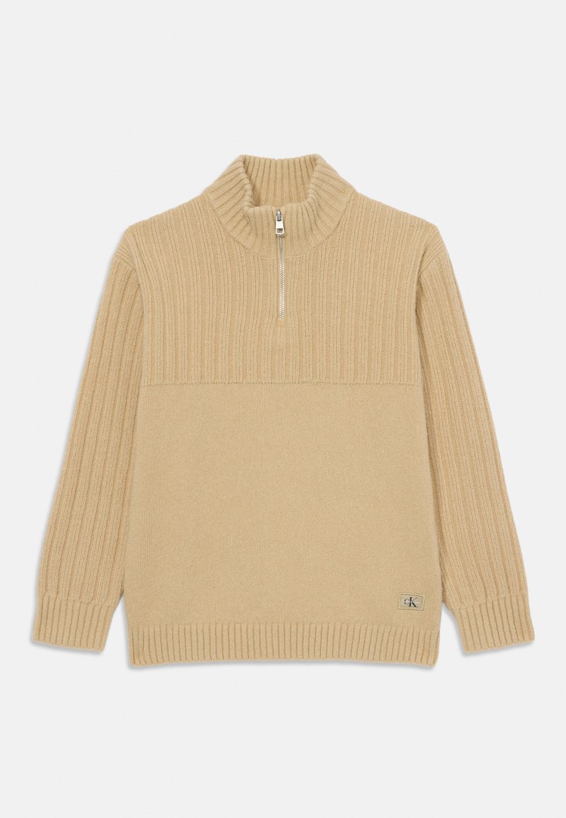 Beige zip-necksweater med ribbet tekstur, lange ermer og en glatt underdel. Har en liten logomerke på kanten.