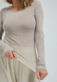 Ljus beige långärmad topp i mjukt tyg, med rund halsringning och lätt textur, tillsammans med en flödande, ljus kjol.