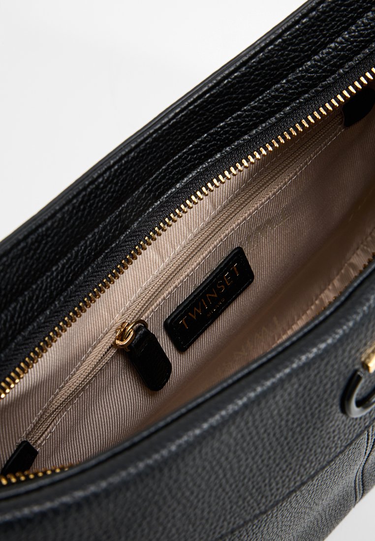 Bolso de mano de cuero negro con superficie texturizada, detalles en cremallera dorada y un interior beige que incluye un bolsillo con cremallera y una etiqueta de la marca.