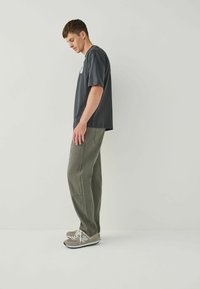 Dark gray T-shirt with short sleeves paired with olive green straight-leg pants and gray sneakers, featuring a logo on the shirt.