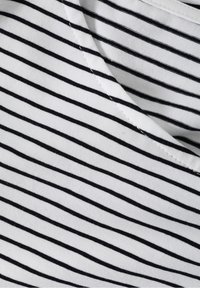 Tela a rayas en blanco y negro, con finas líneas verticales, textura suave y un escote redondo con costuras reforzadas.