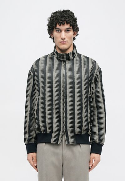 Schwarze und graue Bomberjacke mit einem strukturierten Zickzackmuster, ausgestattet mit einem hohen Kragen und gerippten Bündchen, Reißverschluss und lockerer Passform.