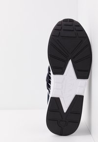 Czarna gumowa podeszwa z teksturowanym wzorem; granatowa cholewka z białymi akcentami i sznurówkami; trójkątne logo na pięcie.