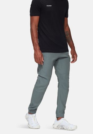 Zwarte lichtgewicht t-shirt met wit logo, gecombineerd met grijze broek met elastische manchetten en witte sportschoenen met een gestructureerd patroon.