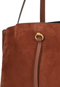 Borsa tote in suede marrone con una finitura liscia, caratterizzata da un accento in metallo dorato e una sottile tracolla in pelle.