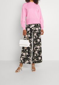 Rosa stickad tröja, blommönstrade vida byxor i svart och rosa, vit handväska med kedjestropp och vit högklackad sandal med remmar.